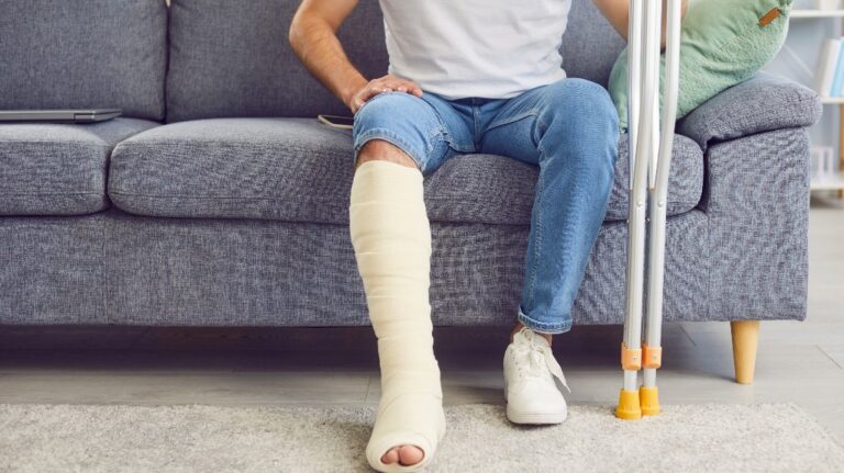 A man with a broken leg sits on the sofa in the living room