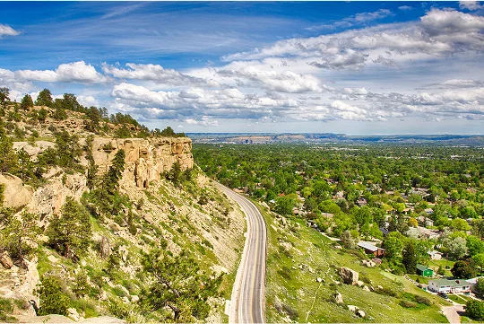 a road on a hill with trees and a city in the background