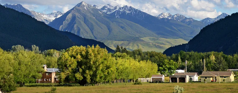 a house in a field with trees and mountains in the background