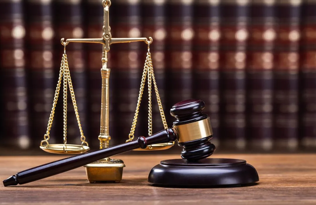 Golden scales of justice and wooden judge's gavel on desk with blurred law books background.