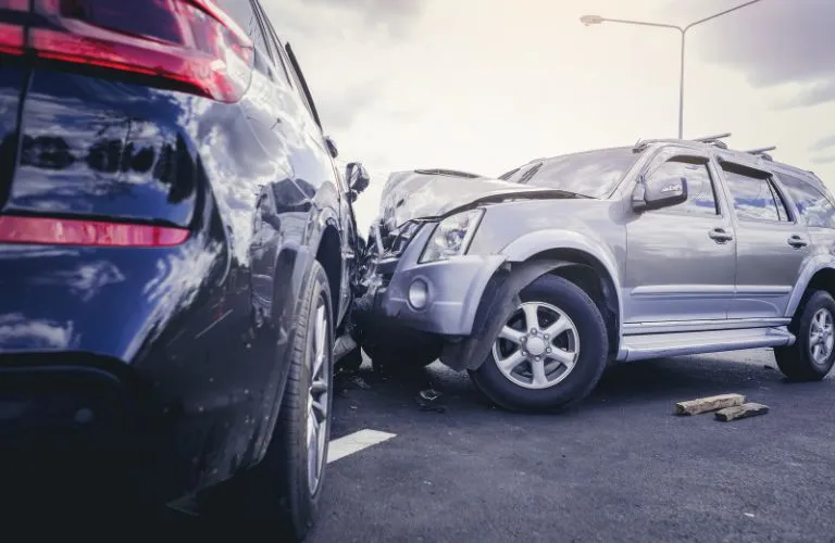 Two SUVs, one black and one silver, involved in a front-end collision on a paved road.