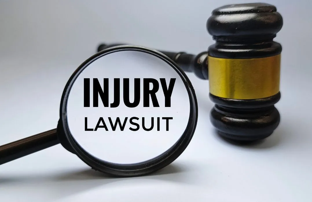 Magnifying glass highlighting the words "INJURY LAWSUIT" next to a wooden judge's gavel.