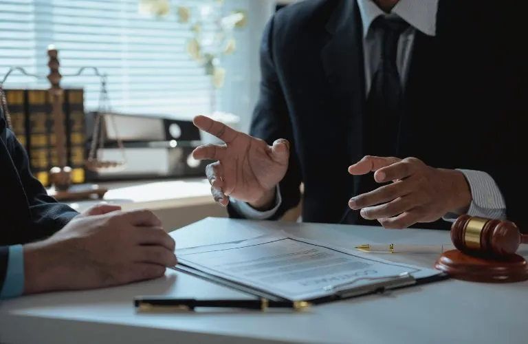 Two professionals in dark suits discussing documents at a desk with a gavel and pen.