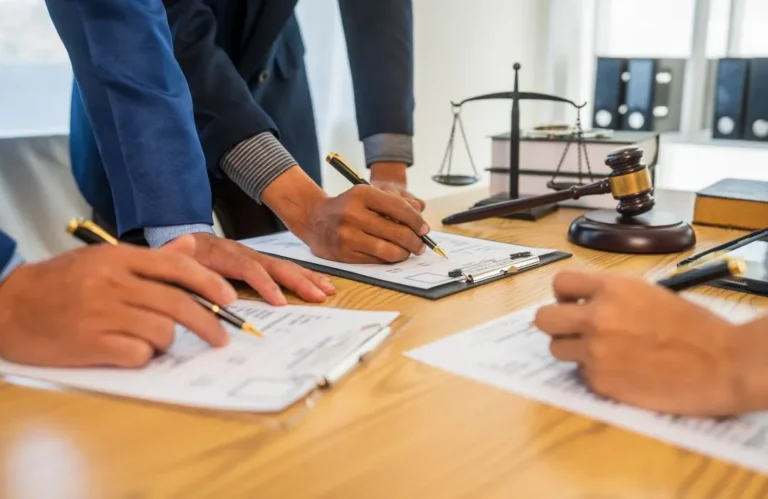 Three individuals in formal attire reviewing and signing legal documents at a wooden desk.
