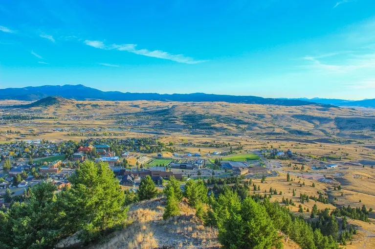 Aerial view of a small town surrounded by dry hills and green trees under a clear blue sky.